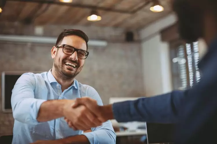 Um vendedor sorridente apertando a mão de um novo cliente.