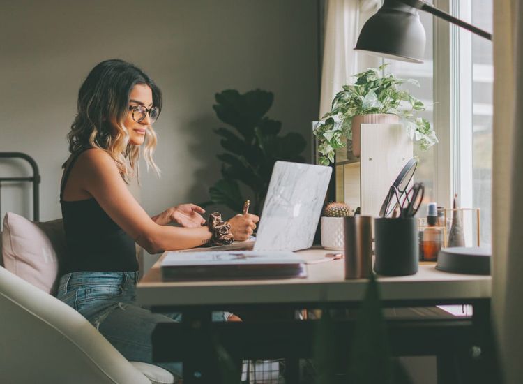 Uma mulher loira e jovem, usando óculos, trabalha em seu notebook.