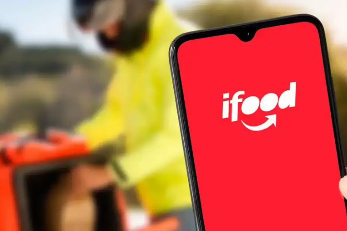 Uma pessoa segura um celular onde se pode ver a marca do ifood e ao fundo a imagem de um entregador, ilustra nosso artigo sobre: Telefone do iFood - Canais de atendimento da plataforma. Foto: Divulgação/iFood Uma pessoa segura um celular onde se pode ver a marca do ifood e ao fundo a imagem de um entregador, ilustra nosso artigo sobre: Telefone do iFood - Canais de atendimento da plataforma. Foto: Divulgação/iFood