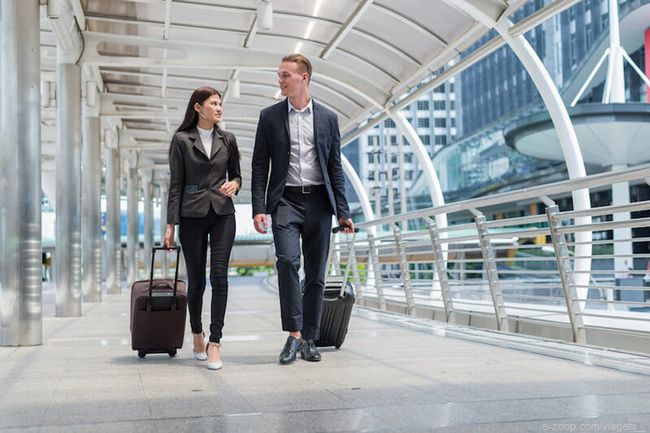 Duas pessoas caminhando e puxando suas malas no saguão de um aéroporto. 