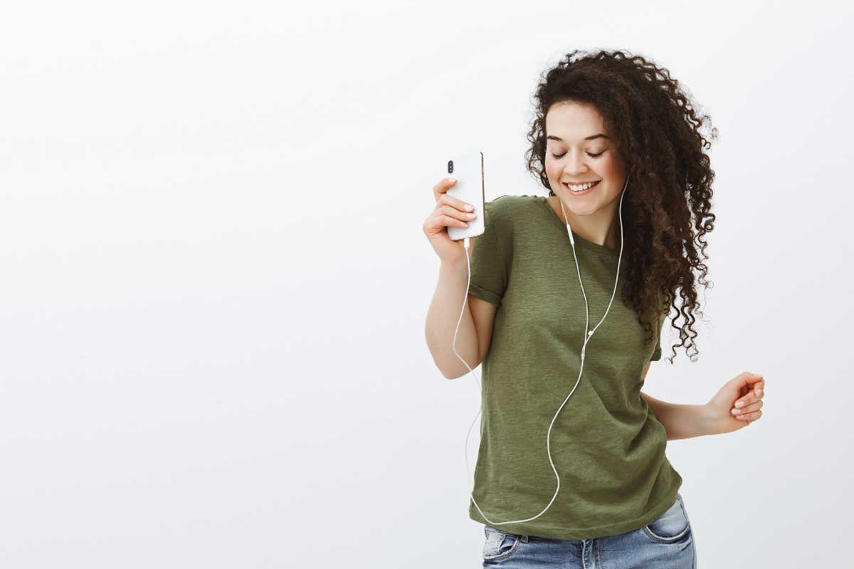 Uma mulher dança ao ouvir música no celular ilustra nosso artigo sobre: Como adicionar toques personalizados no Android. Créditos da Image: Freepik.com